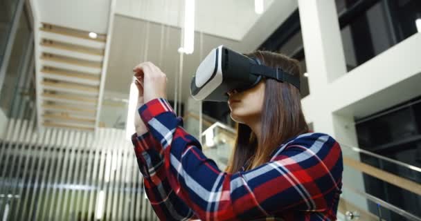 Gros plan de la jeune femme aux cheveux longs et portant dans la chemise bigarrée défilant, tapant et zoomant tout en ayant un casque VR en l'air. Grand hall blanc à l'arrière-plan. Prise de vue portrait. À l'intérieur — Video