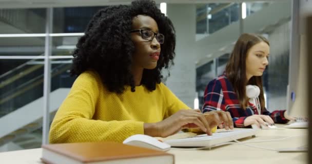 Mujeres multiétnicas que trabajan juntas en las computadoras en la oficina moderna y consultan entre sí. Por la noche. De interior — Vídeo de stock