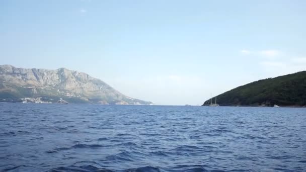 Vista desde el barco sobre el mar con pocas olas. Altas montañas rocosas con pequeños pueblos en la línea del horizonte. Día soleado. Afuera. — Vídeo de stock