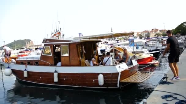 Budva - 10 sierpnia 2017: Człowiek uwolnienia ładne drewniane łódź turyści z molo pełne łodzi do rozpoczęcia rejsu. Kurort w słoneczny letni dzień. Na zewnątrz — Wideo stockowe