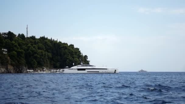 Vista dal mare sul lussuoso yacht bianco che rimane sull'ancora vicino alla bellissima riva rocciosa con alberi verdi. Fuori. — Video Stock