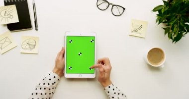 Üstten Görünüm Ofis Masası ve yeşil ekran ve eller üzerinde kayıt olan beyaz tablet bilgisayar. Dikey. Başı işleri ve kahve yanında. Chroma anahtar. Hareket izleme