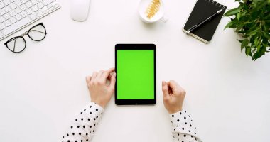 Üstten Görünüm beyaz Ofis Masası ve yeşil ekran ve eller üzerinde kayıt olan siyah tablet bilgisayar. Dikey. Yanında başı işleri. Chroma anahtar.