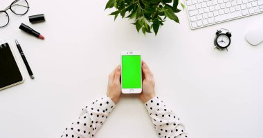 Üstten Görünüm beyaz Ofis Masası ve beyaz Smartphone ile yeşil perde ve eller üzerinde kayıt. Dikey. Yanında başı işleri. Chroma anahtar.