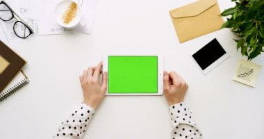 Üstten Görünüm beyaz Ofis Masası ve yeşil ekran ve eller üzerinde kayıt olan beyaz tablet bilgisayar. Yatay. Yanında başı işleri. Chroma anahtar.
