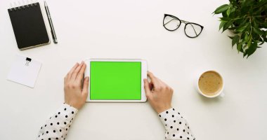 Üstten Görünüm Ofis Masası ve yeşil ekran ve eller üzerinde kayıt olan beyaz tablet bilgisayar. Yatay. Başı işleri ve kahve yanında. Chroma anahtar.