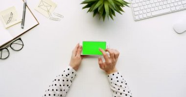 Üstten Görünüm beyaz Ofis Masası ve beyaz Smartphone ile yeşil perde ve eller üzerinde kayıt. Yatay. Yanında başı işleri. Chroma anahtar.