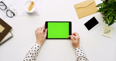 Üstten Görünüm beyaz Ofis Masası ve yeşil ekran ve eller üzerinde kayıt olan siyah tablet bilgisayar. Yatay. Yanında başı işleri. Chroma anahtar.