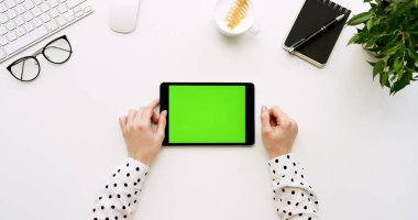 Üstten Görünüm beyaz Ofis Masası ve yeşil ekran ve eller üzerinde kayıt olan siyah tablet bilgisayar. Yatay. Yanında başı işleri. Chroma anahtar.