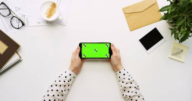 Üstten Görünüm beyaz Ofis Masası ve yeşil ekran ve üzerinde taping eller ile siyah smartphone. Yatay. Yanında başı işleri. Chroma anahtar. Ttracking hareket