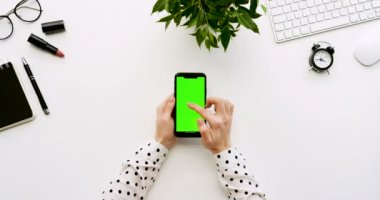 Üstten Görünüm beyaz Ofis Masası ve yeşil ekran ve üzerinde taping eller ile siyah smartphone. Dikey. Yanında başı işleri. Chroma anahtar.