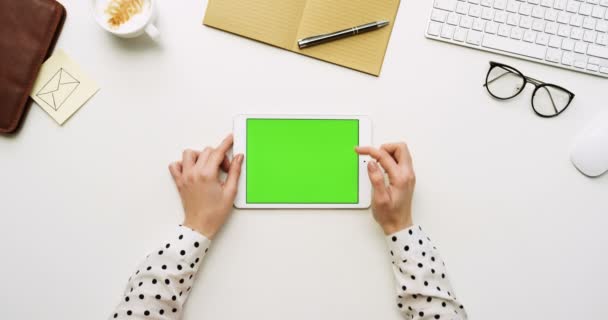 Vista superior en el escritorio de la oficina blanca y tableta blanca con pantalla verde y manos femeninas pegadas en ella. Horizontal. Cosas de oficina al lado. Clave de croma . — Vídeos de Stock