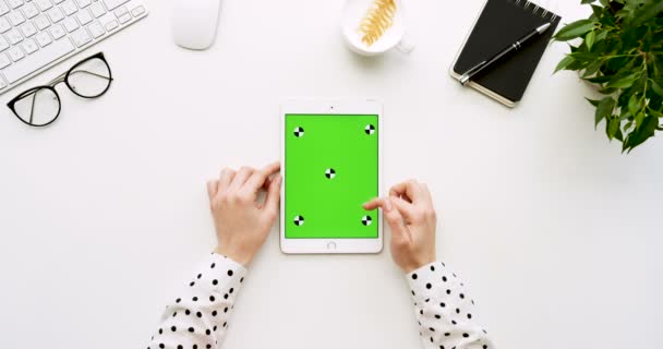 흰색 사무실 책상 및 녹색 스크린 및 여성의 손에 그것에 찍고 흰색 태블릿 컴퓨터에 최고 볼 수 있습니다. 수직입니다. 옆에 사무실 물건입니다. 크로마 키입니다. 모션 추적 — 비디오