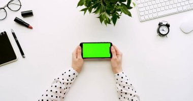 Üstten Görünüm beyaz Ofis Masası ve yeşil ekran ve üzerinde taping eller ile siyah smartphone. Yatay. Yanında başı işleri. Chroma anahtar.