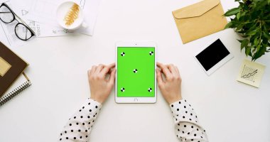 Üstten Görünüm beyaz Ofis Masası ve yeşil ekran ve eller üzerinde kayıt olan beyaz tablet bilgisayar. Dikey. Yanında başı işleri. Chroma anahtar. Hareket izleme