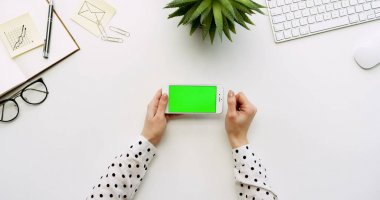 Üstten Görünüm beyaz Ofis Masası ve beyaz Smartphone ile yeşil perde ve eller üzerinde kayıt. Yatay. Yanında başı işleri. Chroma anahtar.