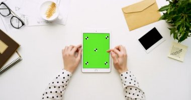 Üstten Görünüm beyaz Ofis Masası ve yeşil ekran ve eller üzerinde kayıt olan beyaz tablet bilgisayar. Dikey. Yanında başı işleri. Chroma anahtar. Hareket izleme