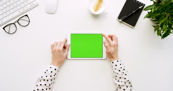 Vista dall'alto sulla scrivania bianca dell'ufficio e sul tablet bianco con schermo verde e con le mani femminili attaccate su di esso. Orizzontale. Roba da ufficio. Chiave cromatica . — Video Stock