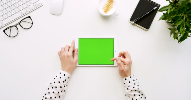 Felülnézet, fehér íróasztal és a zöld képernyő és a női kezek rajta szalagra fehér tabletta számítógép. Vízszintes. Irodai cuccot mellett. Chroma-kulcs. — Stock videók