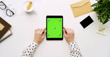 Üstten Görünüm beyaz Ofis Masası ve yeşil ekran ve eller üzerinde kayıt olan siyah tablet bilgisayar. Dikey. Yanında başı işleri. Chroma anahtar. Ttracking hareket