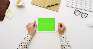 Üstten Görünüm beyaz Ofis Masası ve yeşil ekran ve eller üzerinde kayıt olan beyaz tablet bilgisayar. Yatay. Yanında başı işleri. Chroma anahtar.