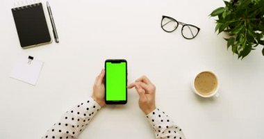 Üstten Görünüm Ofis Masası ve yeşil ekran ve üzerinde taping eller ile siyah smartphone. Dikey. Başı işleri ve kahve yanında. Chroma anahtar.
