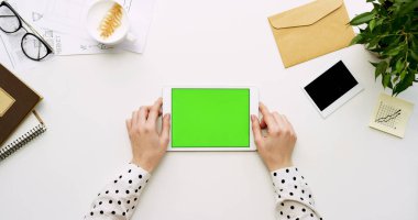 Üstten Görünüm beyaz Ofis Masası ve yeşil ekran ve eller üzerinde kayıt olan beyaz tablet bilgisayar. Yatay. Yanında başı işleri. Chroma anahtar.