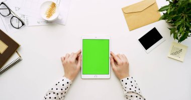 Üstten Görünüm beyaz Ofis Masası ve yeşil ekran ve eller üzerinde kayıt olan beyaz tablet bilgisayar. Dikey. Yanında başı işleri. Chroma anahtar.