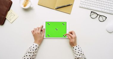 Üstten Görünüm beyaz Ofis Masası ve yeşil ekran ve eller üzerinde kayıt olan beyaz tablet bilgisayar. Yatay. Yanında başı işleri. Chroma anahtar. Hareket izleme