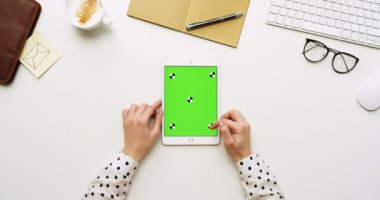 Üstten Görünüm beyaz Ofis Masası ve yeşil ekran ve eller üzerinde kayıt olan beyaz tablet bilgisayar. Dikey. Yanında başı işleri. Chroma anahtar. Hareket izleme