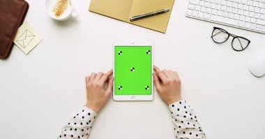 Üstten Görünüm beyaz Ofis Masası ve yeşil ekran ve eller üzerinde kayıt olan beyaz tablet bilgisayar. Dikey. Yanında başı işleri. Chroma anahtar. Hareket izleme
