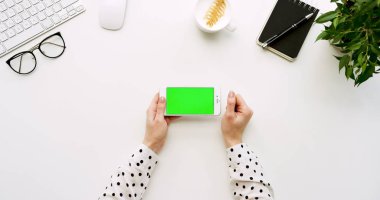 Üstten Görünüm beyaz Ofis Masası ve beyaz Smartphone ile yeşil perde ve eller üzerinde kayıt. Yatay. Yanında başı işleri. Chroma anahtar.