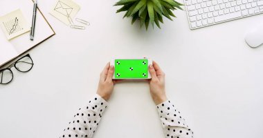 Üstten Görünüm beyaz Ofis Masası ve beyaz Smartphone ile yeşil perde ve eller üzerinde kayıt. Yatay. Yanında başı işleri. Chroma anahtar. Hareket izleme