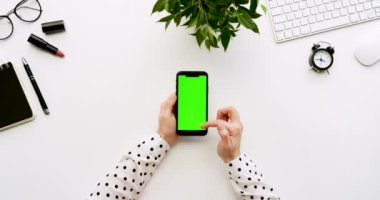 Üstten Görünüm beyaz Ofis Masası ve yeşil ekran ve üzerinde taping eller ile siyah smartphone. Dikey. Yanında başı işleri. Chroma anahtar.