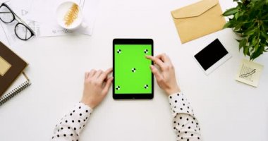 Üstten Görünüm beyaz Ofis Masası ve yeşil ekran ve eller üzerinde kayıt olan siyah tablet bilgisayar. Dikey. Yanında başı işleri. Chroma anahtar. Ttracking hareket
