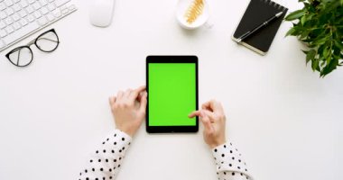Üstten Görünüm beyaz Ofis Masası ve yeşil ekran ve eller üzerinde kayıt olan siyah tablet bilgisayar. Dikey. Yanında başı işleri. Chroma anahtar.