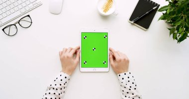 Üstten Görünüm beyaz Ofis Masası ve yeşil ekran ve eller üzerinde kayıt olan beyaz tablet bilgisayar. Dikey. Yanında başı işleri. Chroma anahtar. Hareket izleme