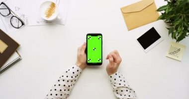 Üstten Görünüm beyaz Ofis Masası ve yeşil ekran ve üzerinde taping eller ile siyah smartphone. Dikey. Yanında başı işleri. Chroma anahtar. Ttracking hareket