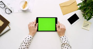 Üstten Görünüm beyaz Ofis Masası ve yeşil ekran ve eller üzerinde kayıt olan siyah tablet bilgisayar. Yatay. Yanında başı işleri. Chroma anahtar.