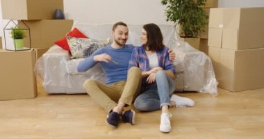 Eğleniyor ve kutuları ve şeyler çevrili otururken onların yeni daire anahtarları tutarak mutlu neşeli genç çift. İçinde