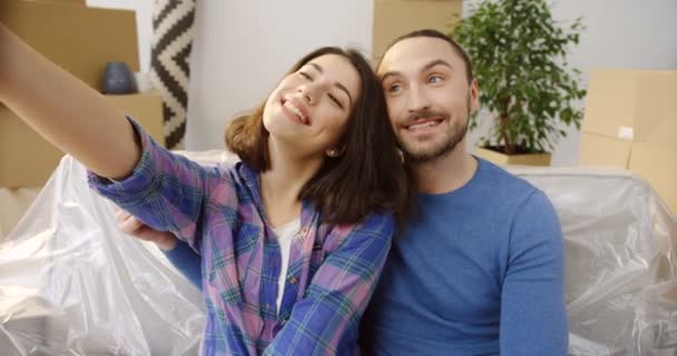 Young cheerful woman and man sitting in the room full of the packed boxes and new stuff whule moving in the new flat and making funny selfies. Close up. Portrait shot. Indoor — Stock Video