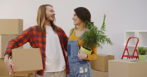 Portrait shot of the young attractive man and woman standing in front of the camera and posing with box and plant in hands. Moving in. Inside — Stock Video