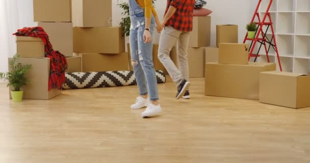 Close up of the feet stepping in new flat. Camera rolling up to the nice young couple being happy in the middle of the boxes and stuff in the cozy light room when moving in. Inside — Stock Video