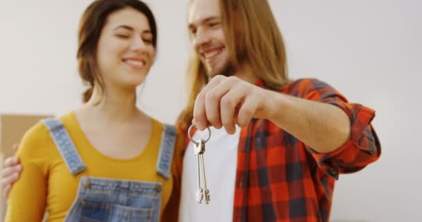 Close-up das chaves de um novo apartamento na mão masculina e casal feliz de jovens proprietários que estão no fundo borrado. Interior — Vídeo de Stock