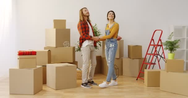 Bara gift ung fru och make hålla händer när du står i mitten av den nya lägenheten full av uppackade lådor och ser sig omkring det. Inomhus — Stockvideo