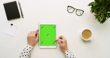 Üstten Görünüm Ofis Masası ve yeşil ekran ve eller üzerinde kayıt olan beyaz tablet bilgisayar. Dikey. Başı işleri ve kahve yanında. Chroma anahtar. Hareket izleme