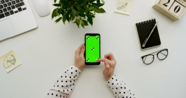 Üstten Görünüm Ofis Masası ve yeşil ekran ve üzerinde taping eller ile siyah smartphone. Dikey. Yanında başı işleri. Chroma anahtar. Hareket izleme