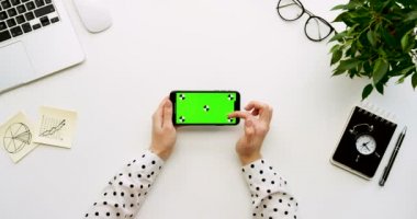 Üstten Görünüm Ofis Masası ve yeşil ekran ve üzerinde taping eller ile siyah smartphone. Yatay. Yanında başı işleri. Chroma anahtar. Hareket izleme