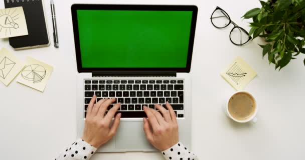 Vista superior de la mesa de la oficina con ordenador portátil con pantalla verde y manos femeninas pegadas en ella. Cuadernos y café al lado. Clave de croma . — Vídeos de Stock