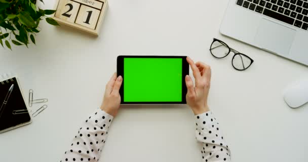 Top view on the office desk and black tablet computer with green screen and female hands taping on it. Horizontal. Office stuff beside. Chroma key. — Stock Video